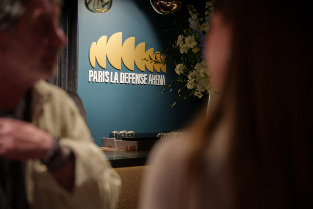 Photo logo Paris La Défense Arena sur le mur d'un salon avec 2 personnes floues
